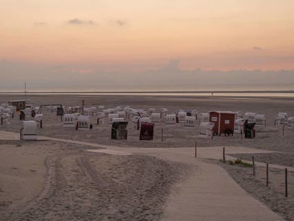 A quiet beach with white beach chairs and a peaceful orange sunset on the horizon, setting sun on a