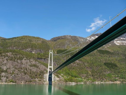 Floating bridge over wooded slopes, under a clear blue sky, bridge in a fjord with snow-capped