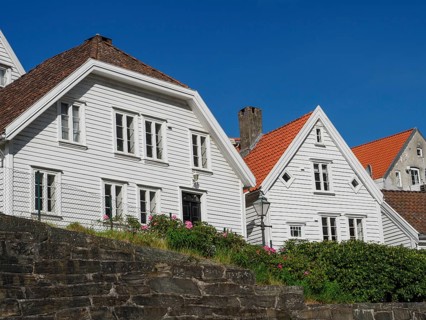 White painted houses with red tiled roofs and flower beds in the front garden, blue sky, stone wall