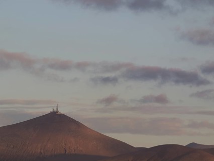 Mountain with antennas on the summit, surrounded by clouds in the soft light of dusk, barren