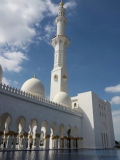 Beautiful mosque with white domes and minarets under a clear blue sky with clouds, large mosque