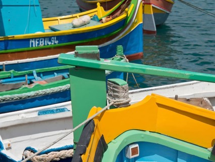 Colourful boats moored side by side at the pier in the clear waters of a harbour, many colourful
