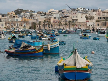 View of a multitude of fishing boats in a busy harbour off the coast of a town, many colourful
