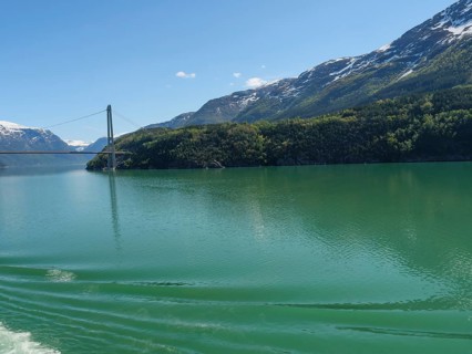View of a bridge over a calm lake, surrounded by snow-capped mountains and dense forests, bridge in