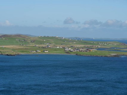 Small settlement with white houses stretches along the grassy coastline in front of the blue sea,