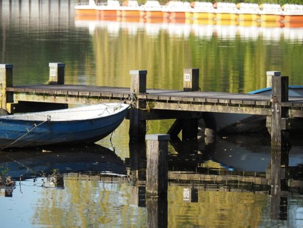 A boat moored on a jetty reflected in the calm waters of a lake, rowing boats and pedal boats on a