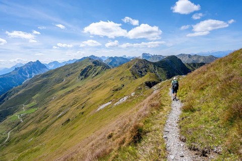 Mountaineer on a hiking trail on a grassy mountain ridge, idyllic mountain landscape with green