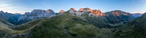 Alpine club hut, mountain landscape with green mountain meadows and rocky peaks at sunrise,