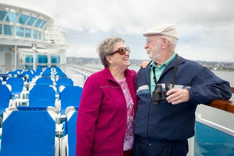 Senior adult couple enjoying the view from their passenger cruise ship with their bonoculars