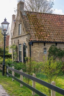 Small brick house with tiled roof and garden, surrounded by fresh spring greenery, rustic