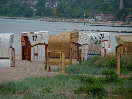 Beach chairs on a sandy beach along the coast, with dense vegetation and houses in the background,