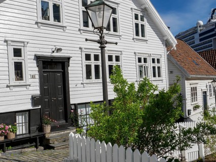 White wooden houses with flowers and black doors along a cobblestone street with a street lamp,