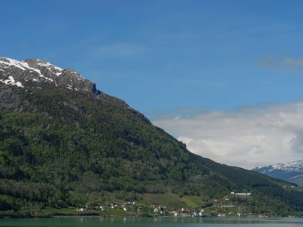 Small settlement in front of a green mountainside and snow-capped peaks under a clear sky, greenish