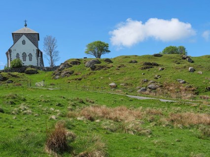 Church with stone tower on hilly landscape under blue sky with clouds, trees in the background, old