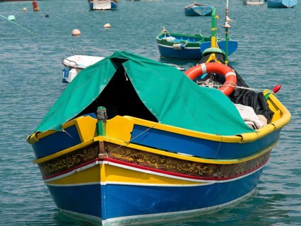 A colourful fishing boat with green fabric cover and lifebuoy at anchor, many colourful fishing
