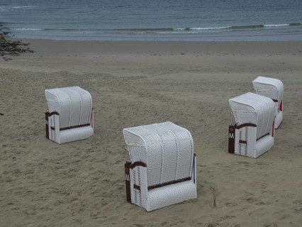 Four white beach chairs on an empty beach with calm sea in the background, beach chairs and beach