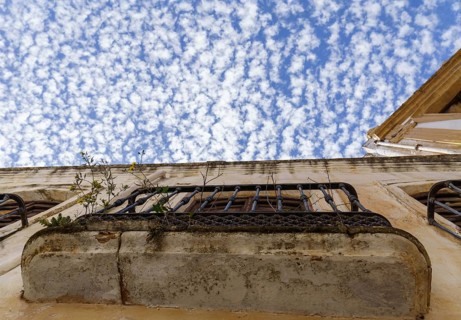 Old rusty, overgrown balcony of an abandoned house with a blue sky and clouds in the background