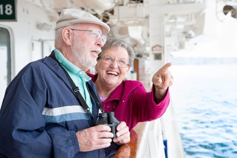 Senior adult couple enjoying the view from their passenger cruise ship with their bonoculars