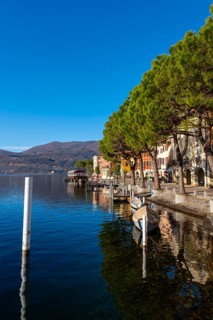 Old Beautiful Town with Building and Trees on the Waterfront on Lake Lugano with Boat in a Sunny