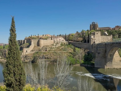 View of a fortress and historic walls over a river with cypress trees and green vegetation under a