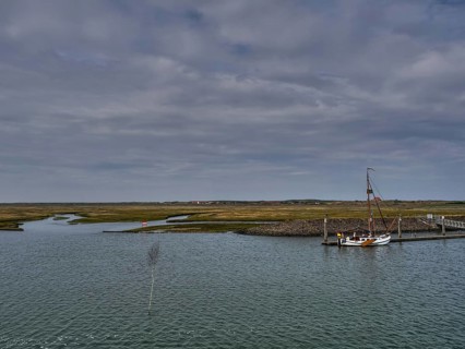 Sailboat at a jetty surrounded by a watery landscape under a cloudy sky, small jetty with a