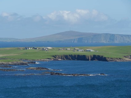 Peaceful coastal landscape with green hills and houses by the blue sea, green meadows by a deep