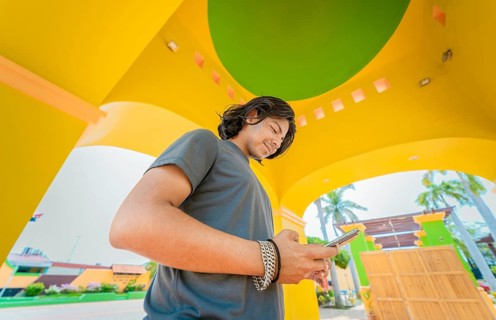 Low angle view of young man using cell phone outdoors. Smiling latin guy texting with cell phone in