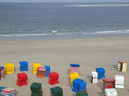Various colourful beach chairs scattered on empty beach with calm sea in background, beach chairs