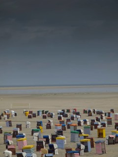 Dramatic sky over numerous colourful beach chairs on empty, wide beach with sea view, beach chairs