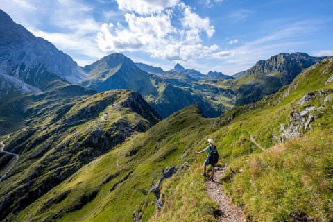 Mountaineer on a hiking trail on a grassy mountain ridge, idyllic mountain landscape with green