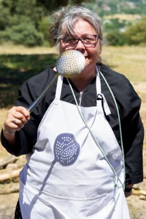Woman cook in white apron with a spatula in her hand smiling in the field