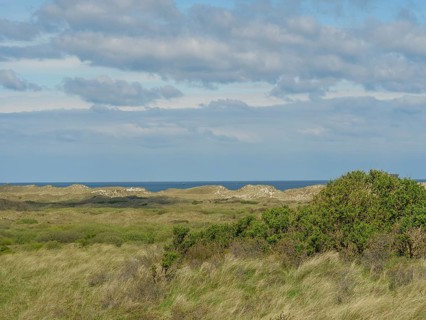 Vast landscape with hills and a view of the sea under a cloudy sky, dune and hiking trails on the