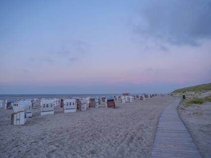 A long beach with white and striped beach chairs in the soft evening light and a wide wooden