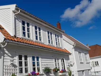 White house with red tiled roof, blooming flowers in the foreground under blue sky, white wooden