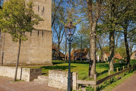 Street lamp next to a brick tower and trees, with a pavement and spring atmosphere, historic houses