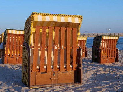 Close-up of a beach chair on the beach with other baskets and a pier in the background, beach