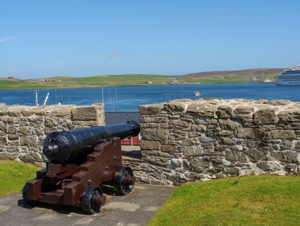 Historic cannon in front of a stone wall with a view of the sea, a ship and green hills, old