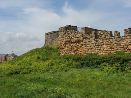 A solid fortress wall on a grassy hill under a blue sky, ruins and old stone walls by the sea,
