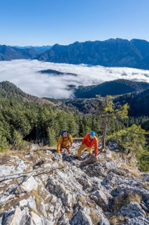 Two friends, mountaineers climbing the via ferrata to the rocky summit of the Ettaler Manndl, view