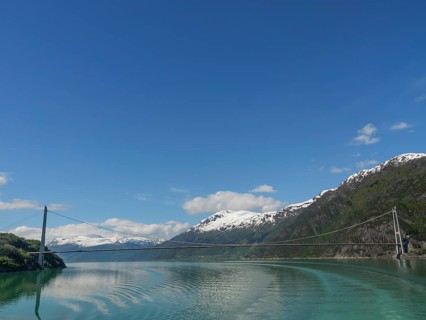 A bridge spans the turquoise water, surrounded by snow-capped mountains under a blue sky, bridge in