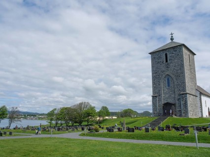 Old church on a cemetery next to a lake under a cloudy sky, old stone church and many gravestones