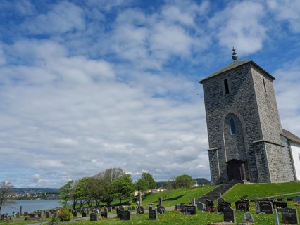 Cemetery with old graves and a church on the shore of a lake under a cloudy sky, old stone church