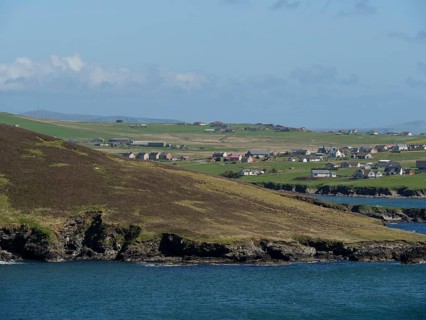 Green fields and houses on a rocky coastline overlooking the sea, green meadows on a deep blue sea