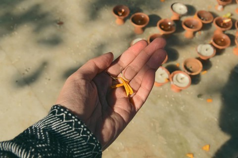 Overhead view of a hand holding several petals from a marigold garland over several tea candles,