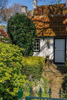 Entrance of a house surrounded by a garden with trees and hedges in spring, brick path, historic