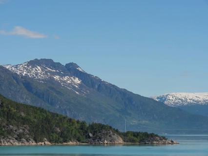 View of steep, forested mountains, a lake and snow-capped peaks in sunny weather, greenish