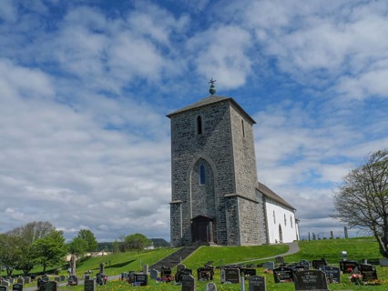 Stone church in a cemetery under a cloudy sky with trees in the background, old stone church and