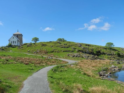 Church in the distance with hiking trail, hilly landscape and blue sky with clouds, old stone
