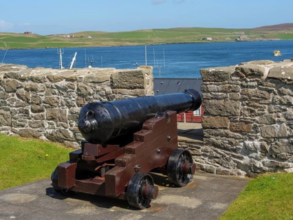 Old cannon in front of a stone wall with a view of the sea and green hills in the background, old