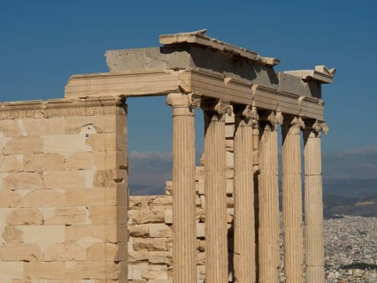 Ancient marble columns in a ruin with a part of the city in the background under a clear sky,